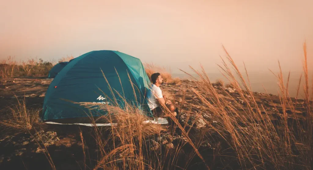 a guy sitting out side of his tent basking in the sun enjoying his camping trip.