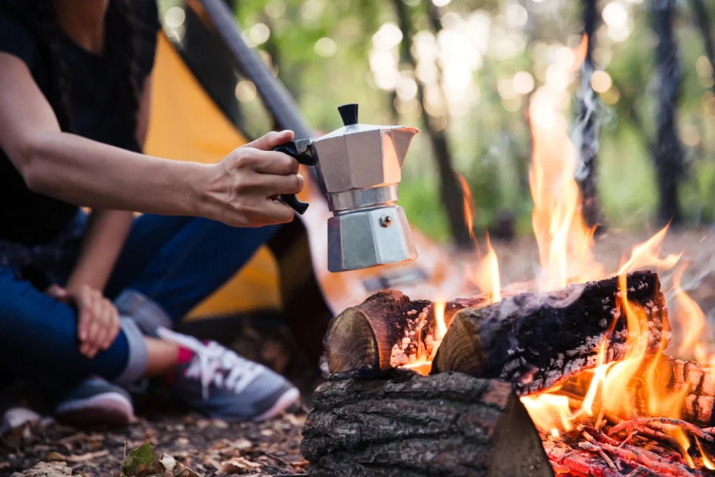 a moka pot being held near a campfire.