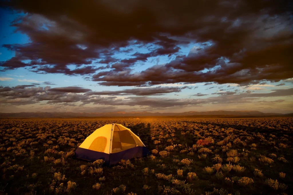 types of camping - a single tent set up in a field at sunset