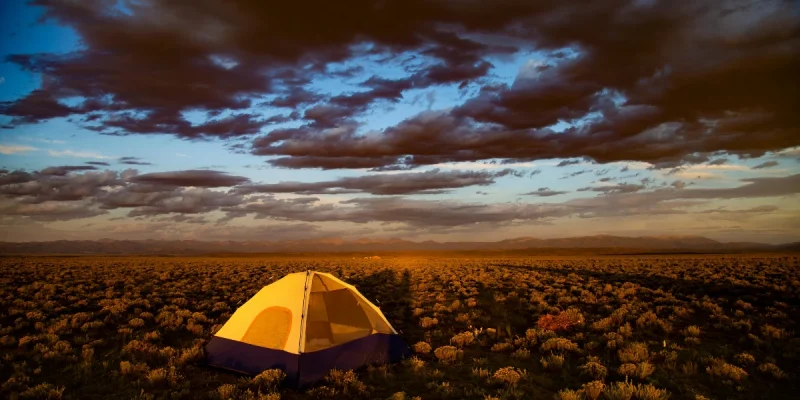 types of camping - a single tent set up in a field at sunset