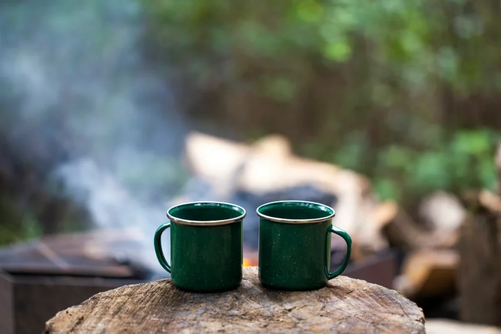 A photo of two green coffee mugs filled with camp coffee at a camp site