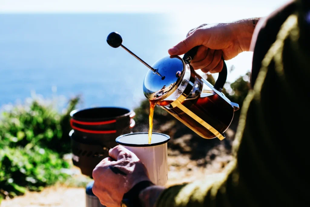 a person making camp coffee with a lightweight french press overlooking the ocean