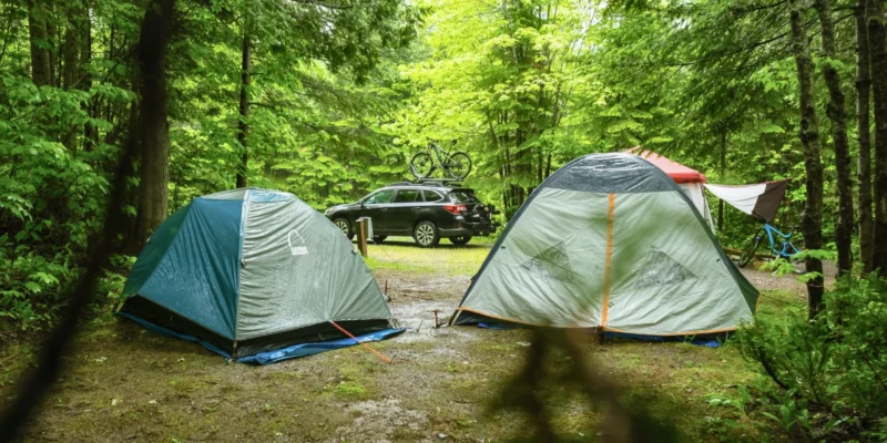 A photo of two tents and vehicle car camping in the rain